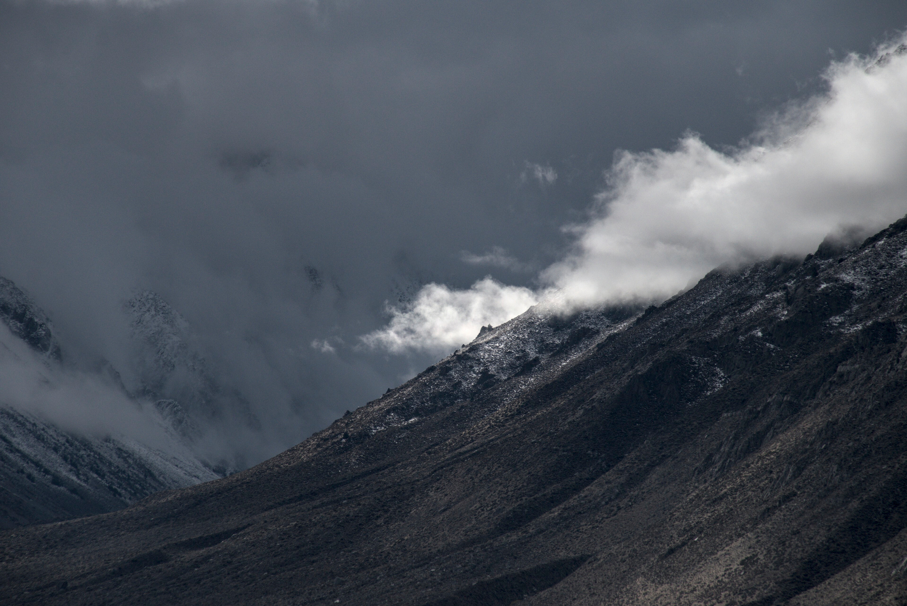 A small cloud, brightly lit from the back by sunlight, pokes out from behind a granite ridge.
