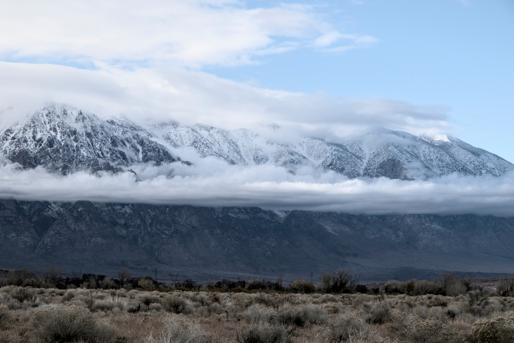 A snow covered granite crest freshly covered with snow looms over a high desert valley floor.