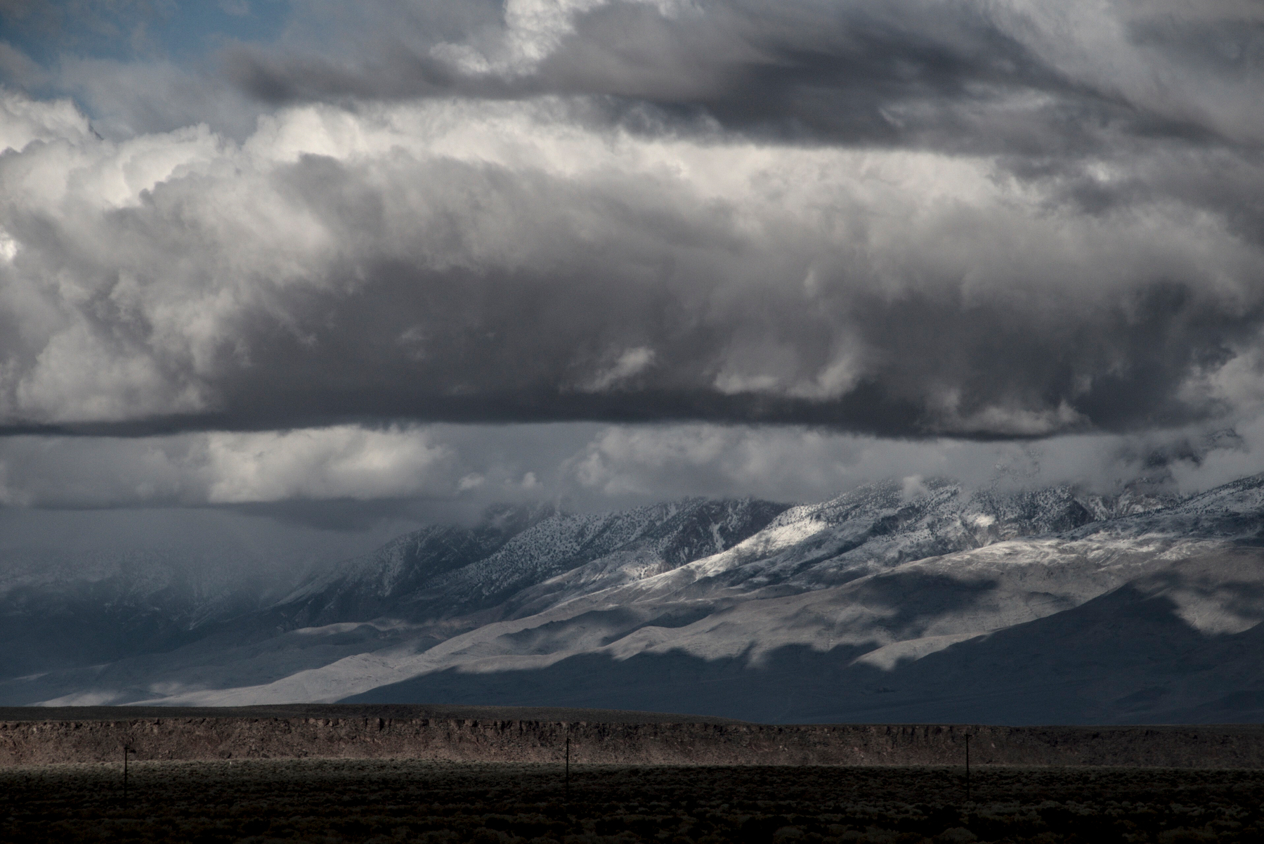 A lng, dark tubular cloud flows out of a mountain canyon.