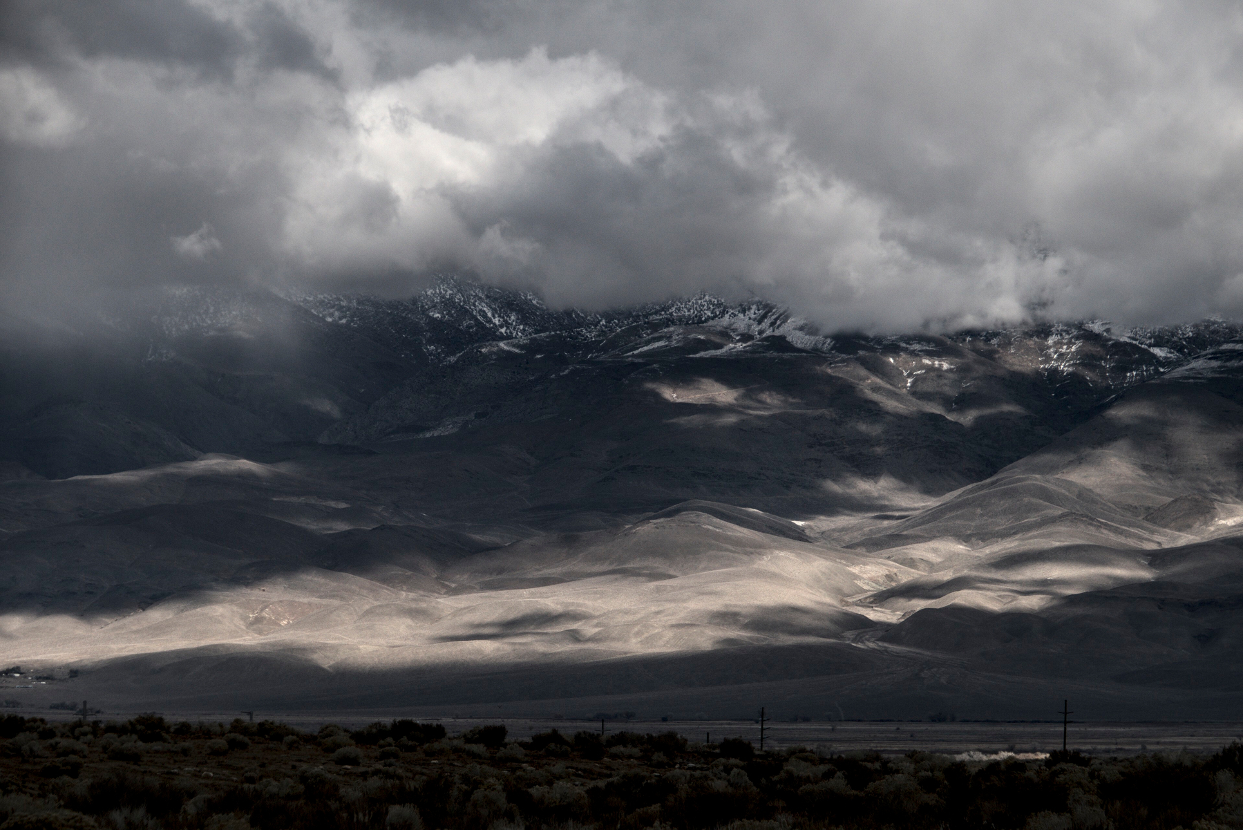 Clouds cover the peaks of a mountain range while incoming clouds cast shadows at their feet.