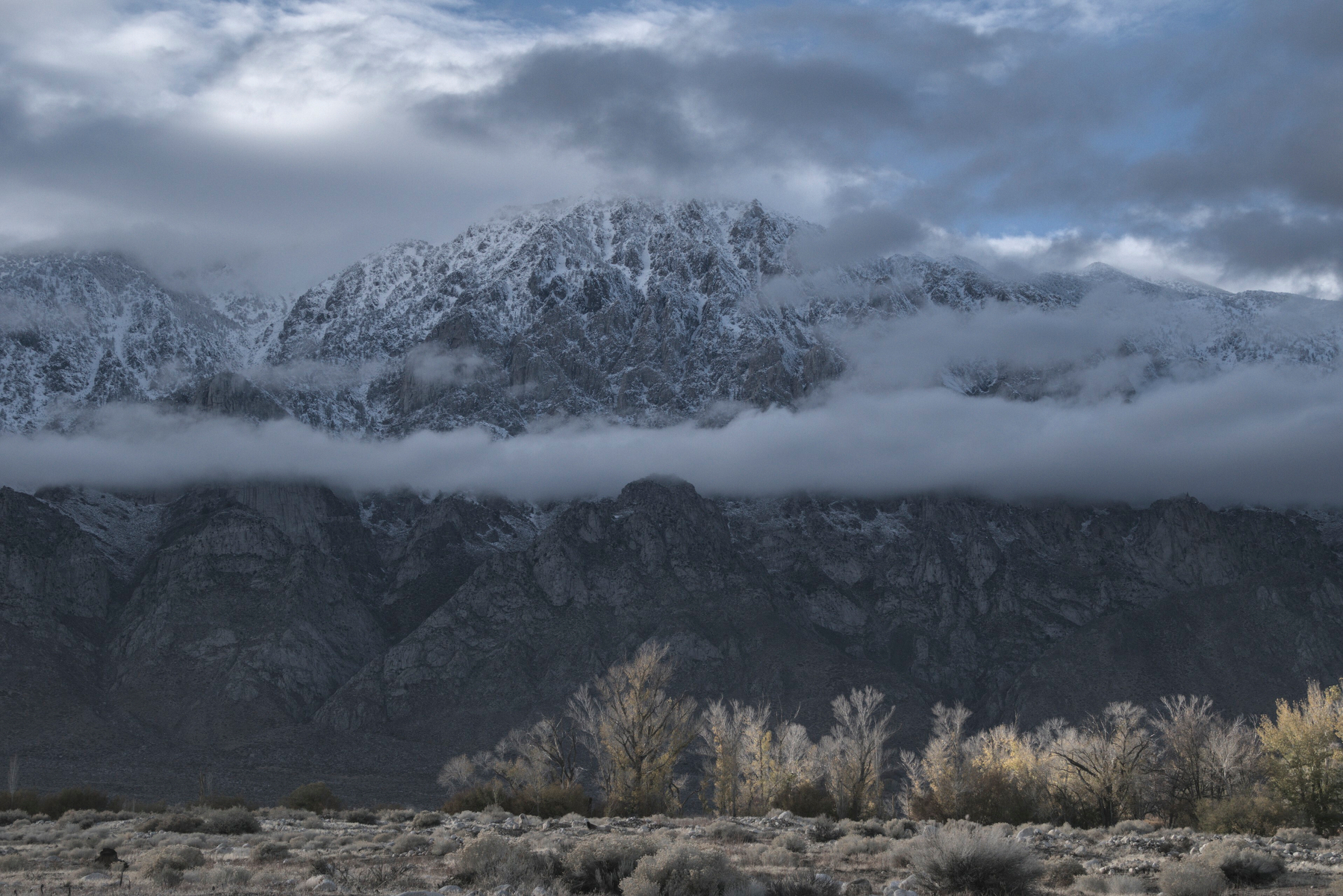 Clouds run along a snow covered granite cliff face.