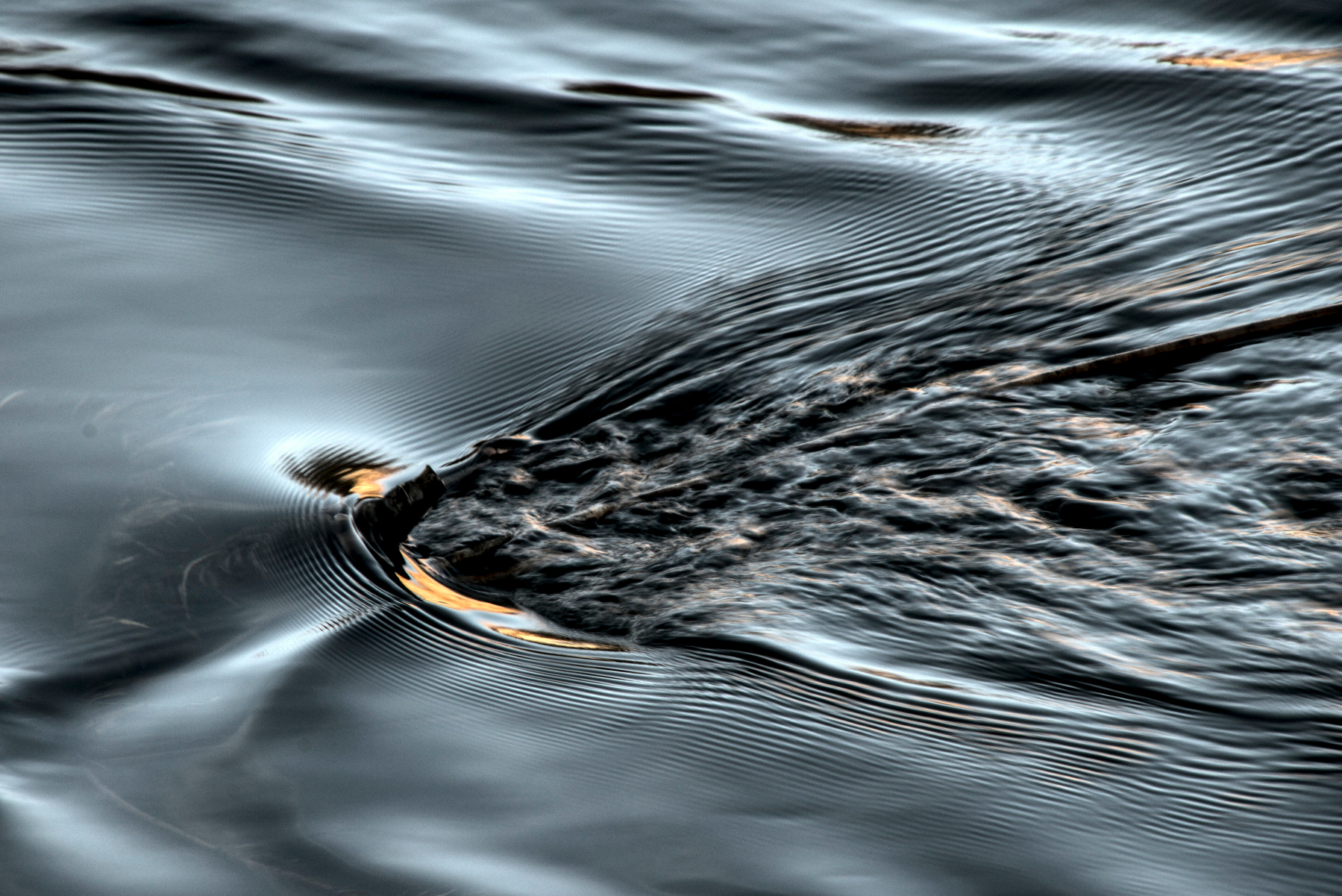 Something submerged in a river generates a complex wave pattern downstream.