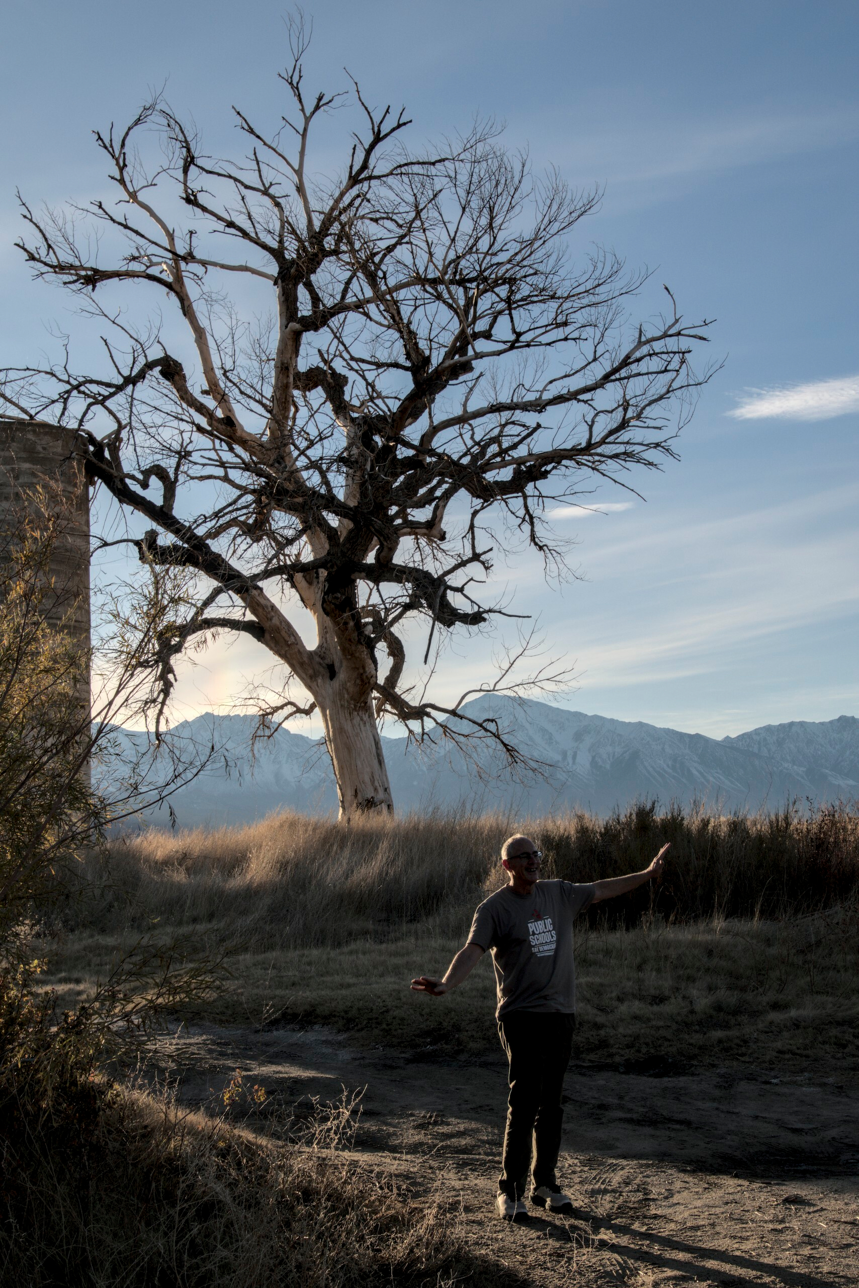 A man poses, imitating the tree behind him, or possibly just taking  selfie.