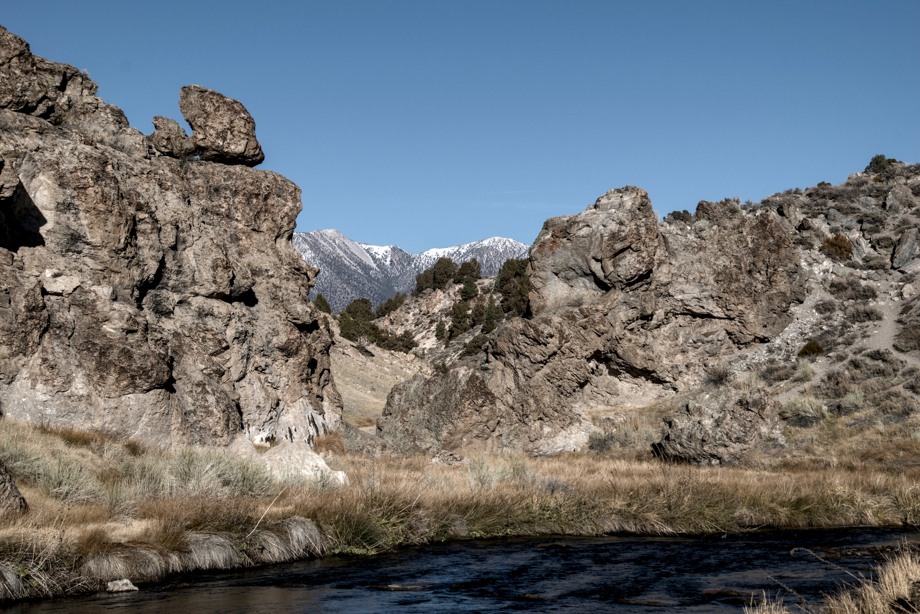 Snow-covered mountains are visible in the distance through a gap in a rocky canyon wall.